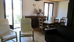 A living room with a sofa, a dining table with chairs, and a kitchen area with cabinets and a window.