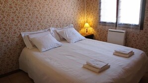 A neatly made bed with white linens and pillows, a bedside lamp, and a radiator.