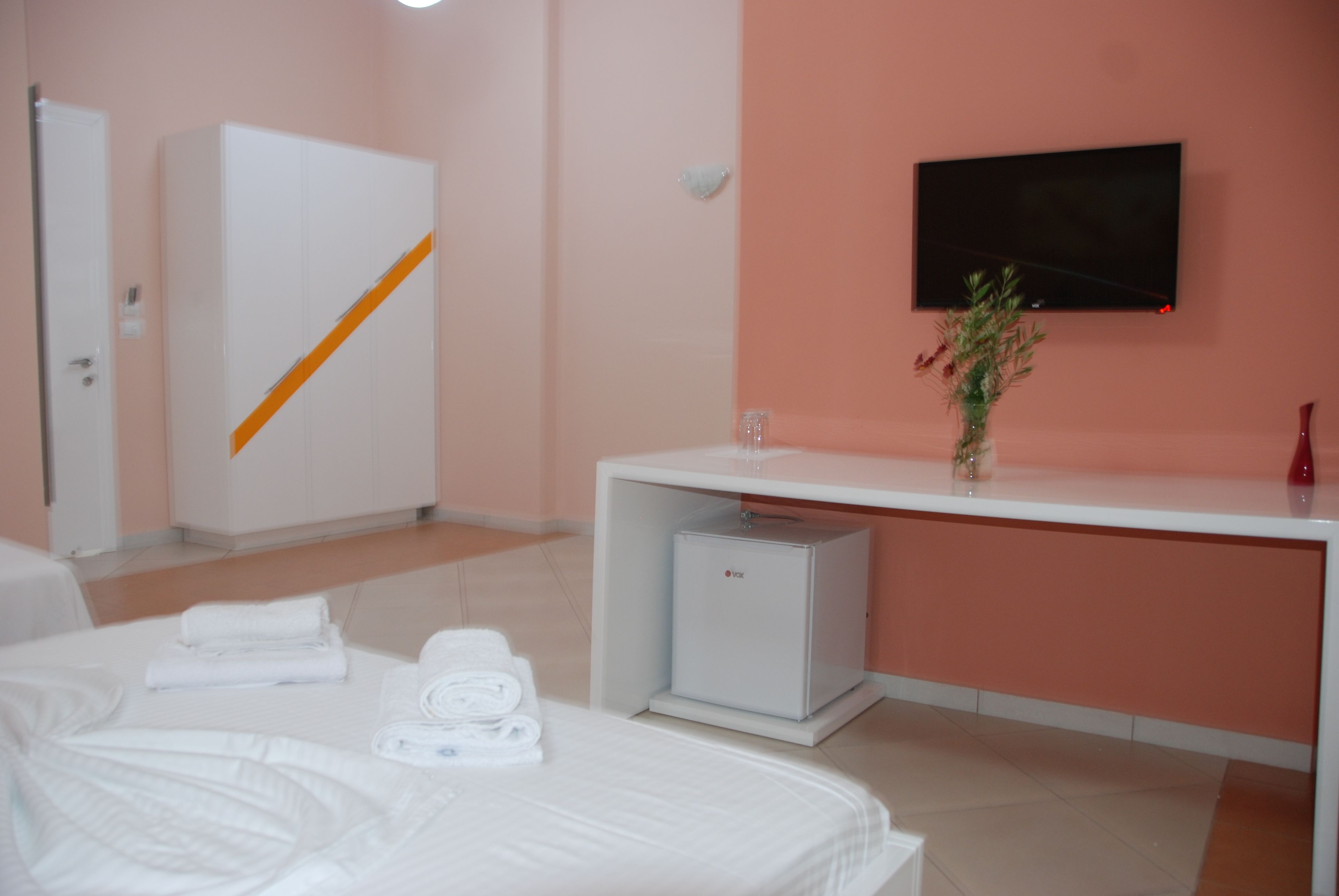 Una habitación de hotel con cama, un armario blanco, un escritorio con televisor de pantalla plana y un refrigerador pequeño.