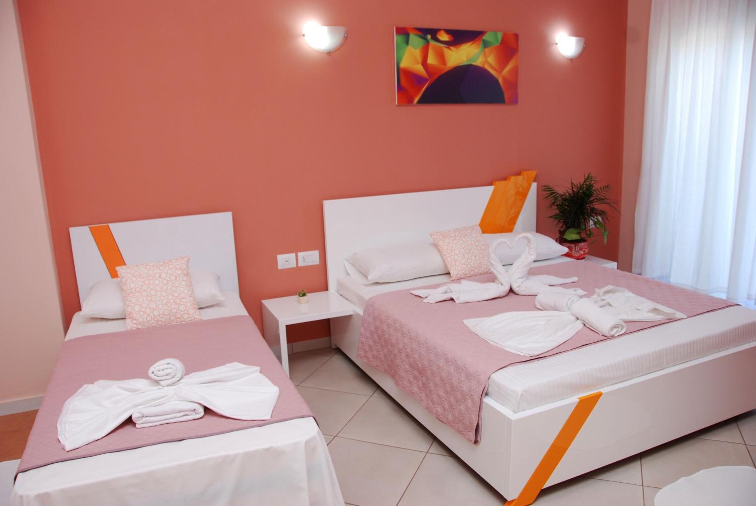 Ein Hotelzimmer mit zwei Betten, jedes mit einer rosafarbenen Tagesdecke und weißen Kissen. Auf jedem Bett liegen ordentlich gefaltete Handtücher.