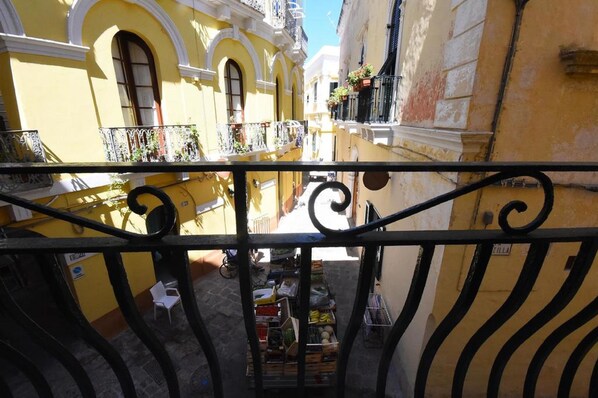 A narrow street with yellow buildings, a balcony with a metal railing, and a small outdoor seating area. - B&B Laura - Luxury Rooms (Gallipoli)