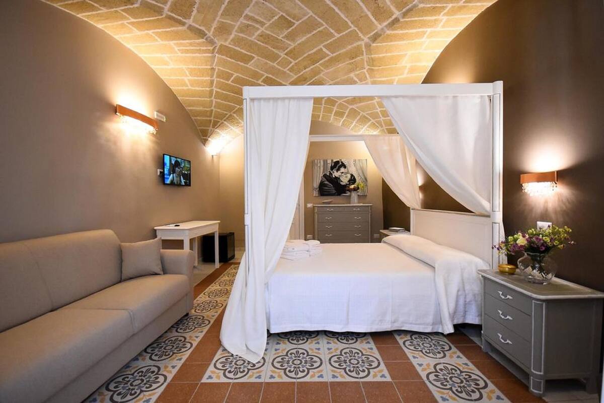 Un dormitorio con una cama, un sofá, una mesita de noche, un televisor y un adorno de pared.