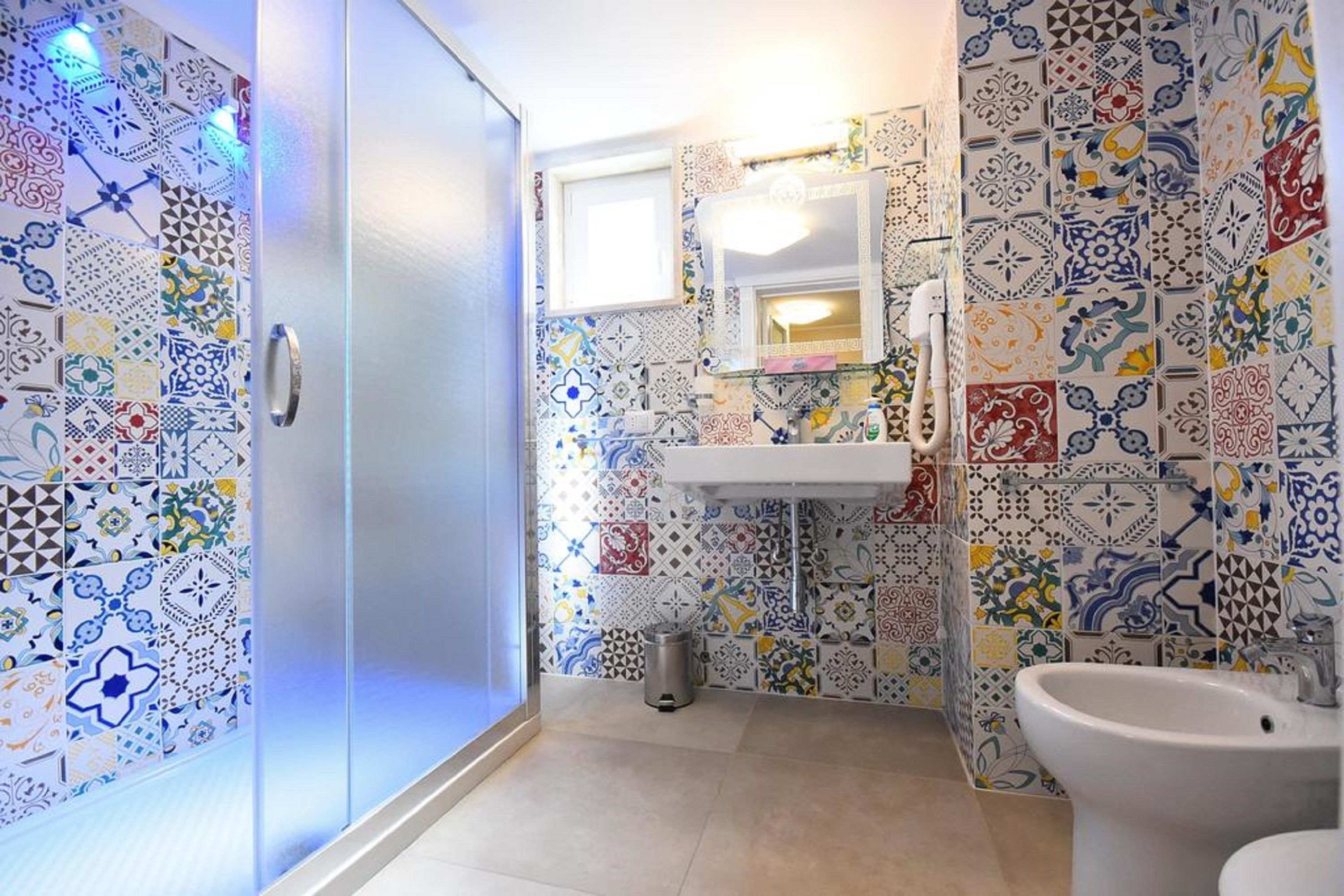 Ein Badezimmer mit gefliesten Wänden, einem Waschbecken, einem Spiegel und einem Bidet.