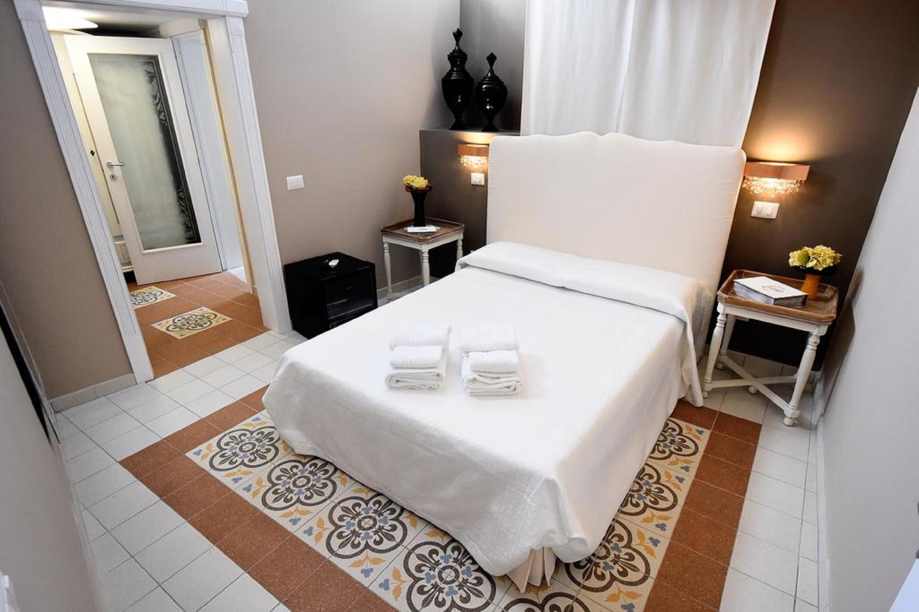 Een hotelkamer met een bed, nachtkastje, spiegel en een deur.