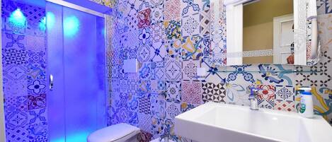 Casa de banho com lavatório branco, bidé e sanita. As paredes estão revestidas de azulejos coloridos e estampados.