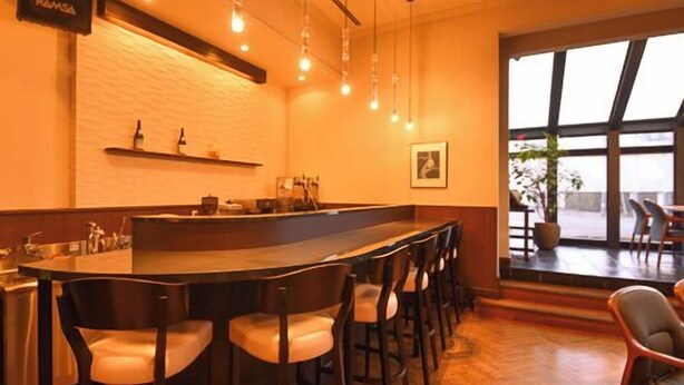 Un espace bar doté d’un long comptoir, de nombreux tabourets et de luminaires suspendus.