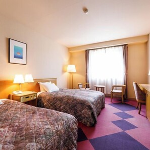 Een hotelkamer met twee bedden, een bureau, een stoel en een raam met gordijnen.