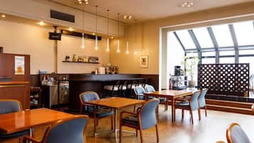 A restaurant interior with wooden tables and chairs, a bar area, and a large window providing natural light.