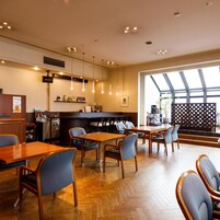 Un interior de restaurante con mesas y sillas de madera, una zona de bar y un amplio ventanal que proporciona luz natural.