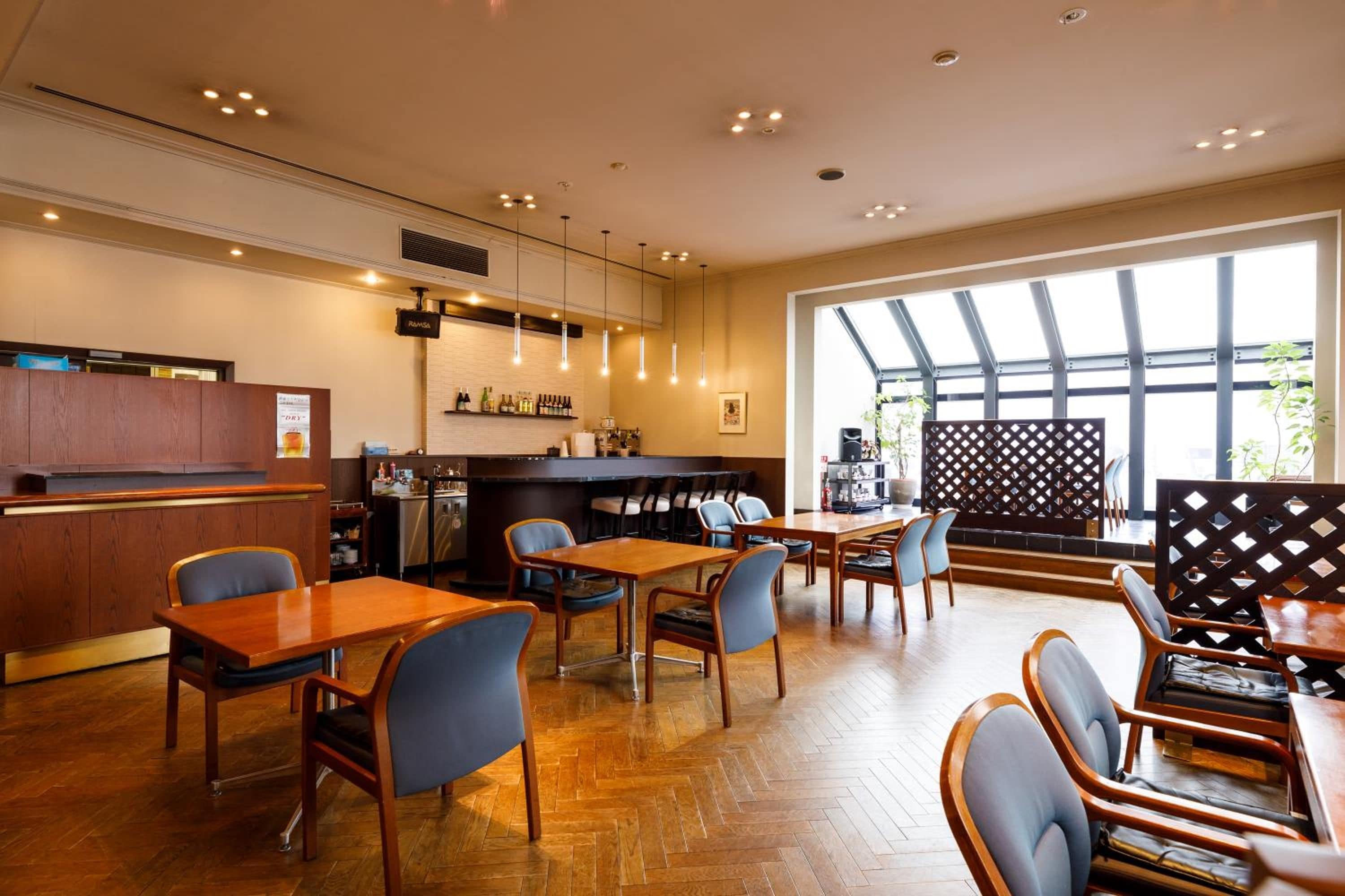 A restaurant with wooden furniture, a bar area, and a large window providing natural light.