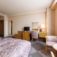 Una habitación de hotel con una cama, un escritorio con computadora, una silla, una mesita y una lámpara.