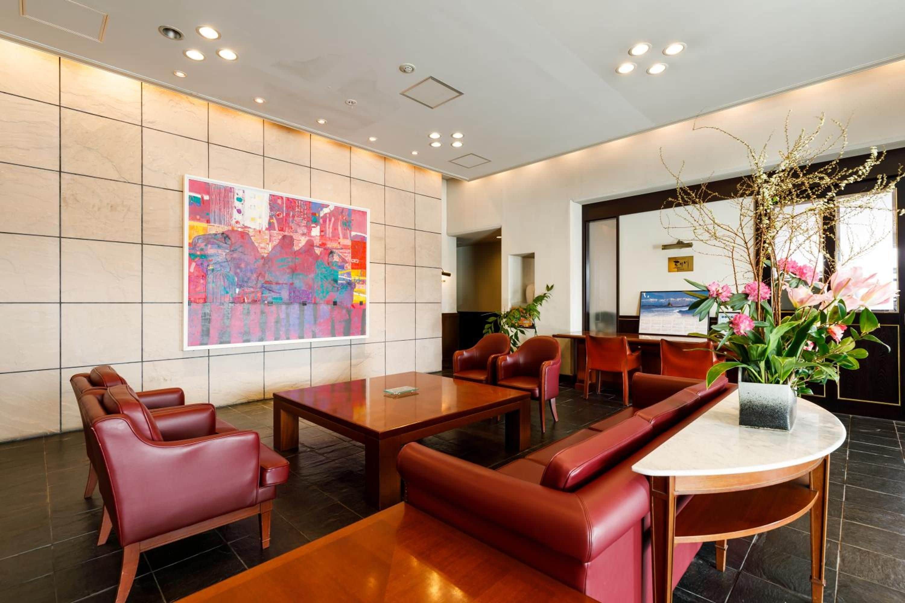 Um hall de hotel com uma grande pintura abstrata, assentos de couro, uma mesa redonda e uma recepção.