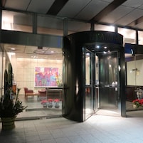 Entrada de hotel con puerta giratoria, fachada de vidrio y una obra de arte colorida en la pared.