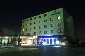 A multi-story hotel with a modern facade, illuminated entrance, and a well-lit parking area.