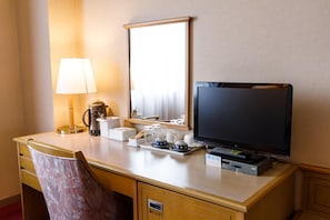 Ein Schreibtisch im Hotelzimmer mit Fernseher, Lampe, Kaffeemaschine und Spiegel.
