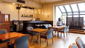 Un restaurant avec des tables et des chaises en bois, un coin bar et une grande fenêtre laissant entrer la lumière naturelle.