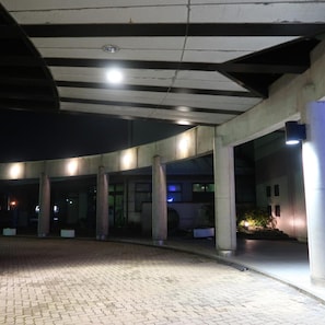 Ein überdachter Außenbereich mit Säulen, einem Backsteinboden und einem Gebäude im Hintergrund.