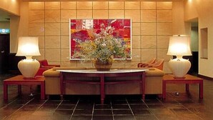 Un hall d’entrée avec une table centrale, deux lampes, un arrangement floral et un grand tableau abstrait accroché au mur.