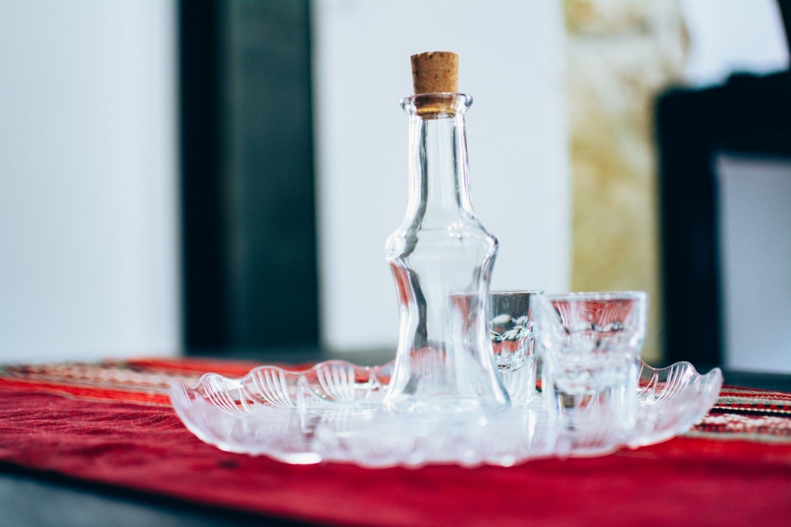 Una botella de vidrio transparente con tapón de corcho sobre un mantel rojo estampado.