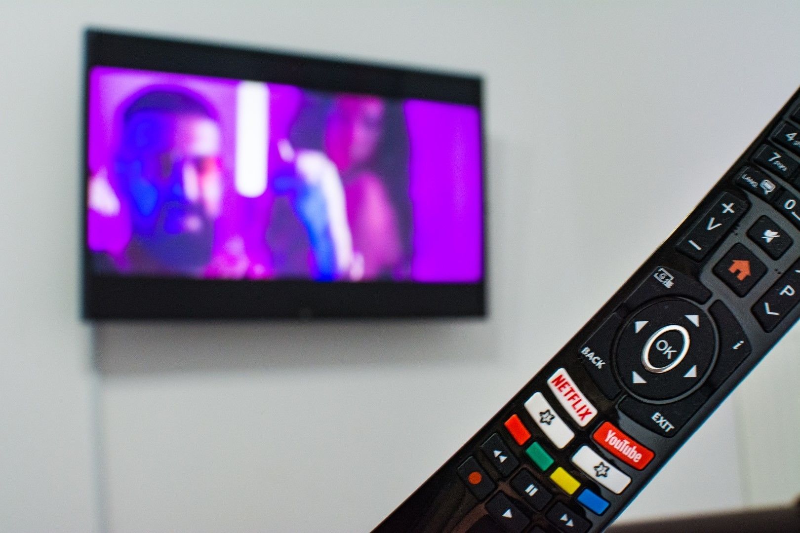 Un téléviseur affiche une scène aux tons violets, et une télécommande est posée au premier plan, avec des boutons indiquant « Netflix » et « YouTube ».