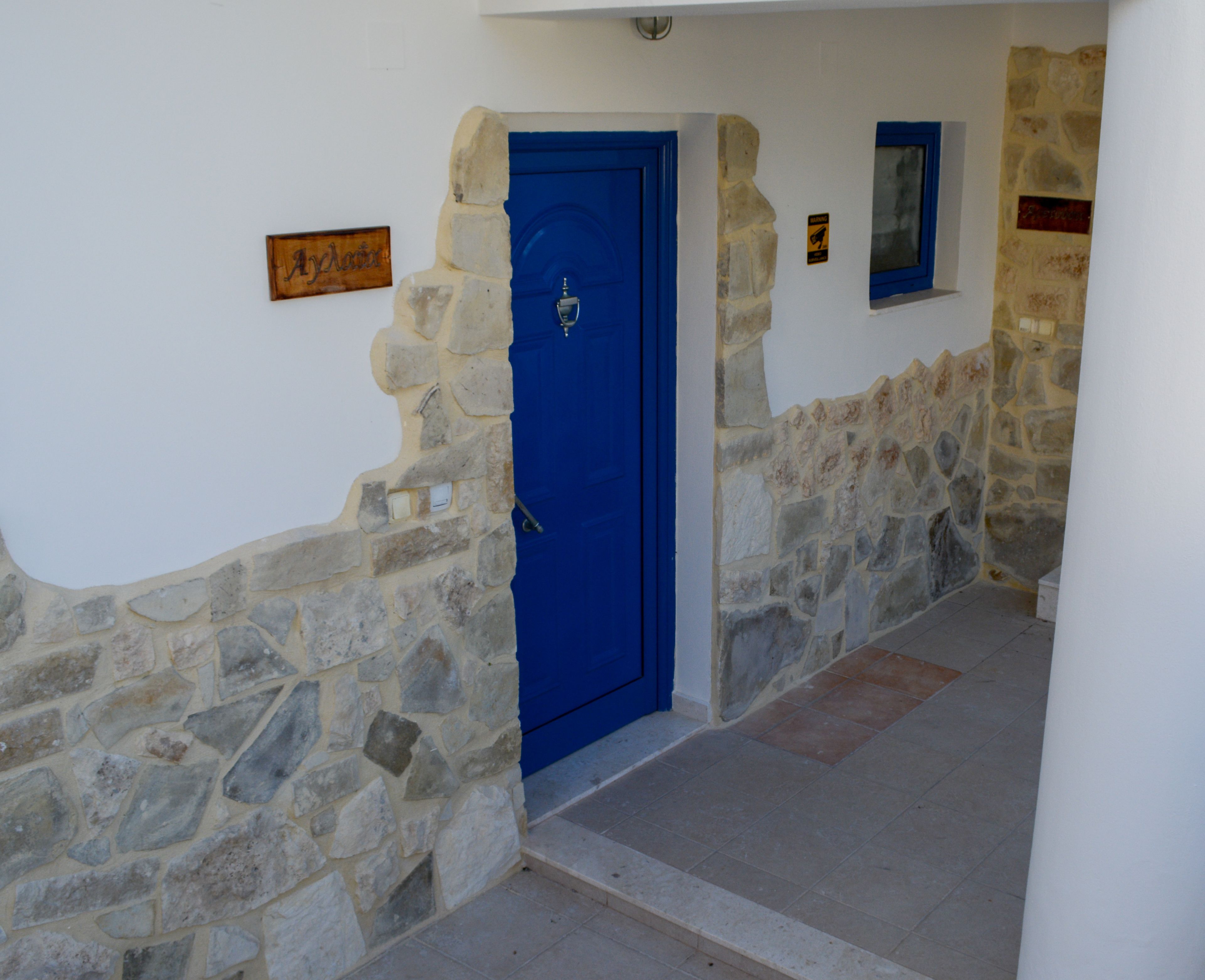A stone wall with a blue door, a sign with a name, and a small window.