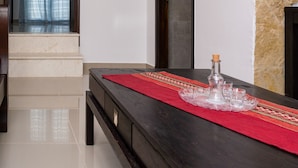 Een eethoek met een houten tafel, een rode tafelkleed en een fles. Twee ingelijste foto's hangen aan de muur.