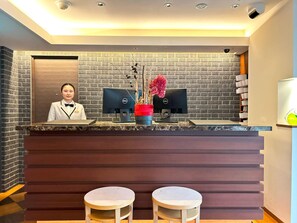 A reception desk with two monitors, a receptionist, and a decorative vase with flowers. - Garden Hotel Shizuoka (Shizuoka)