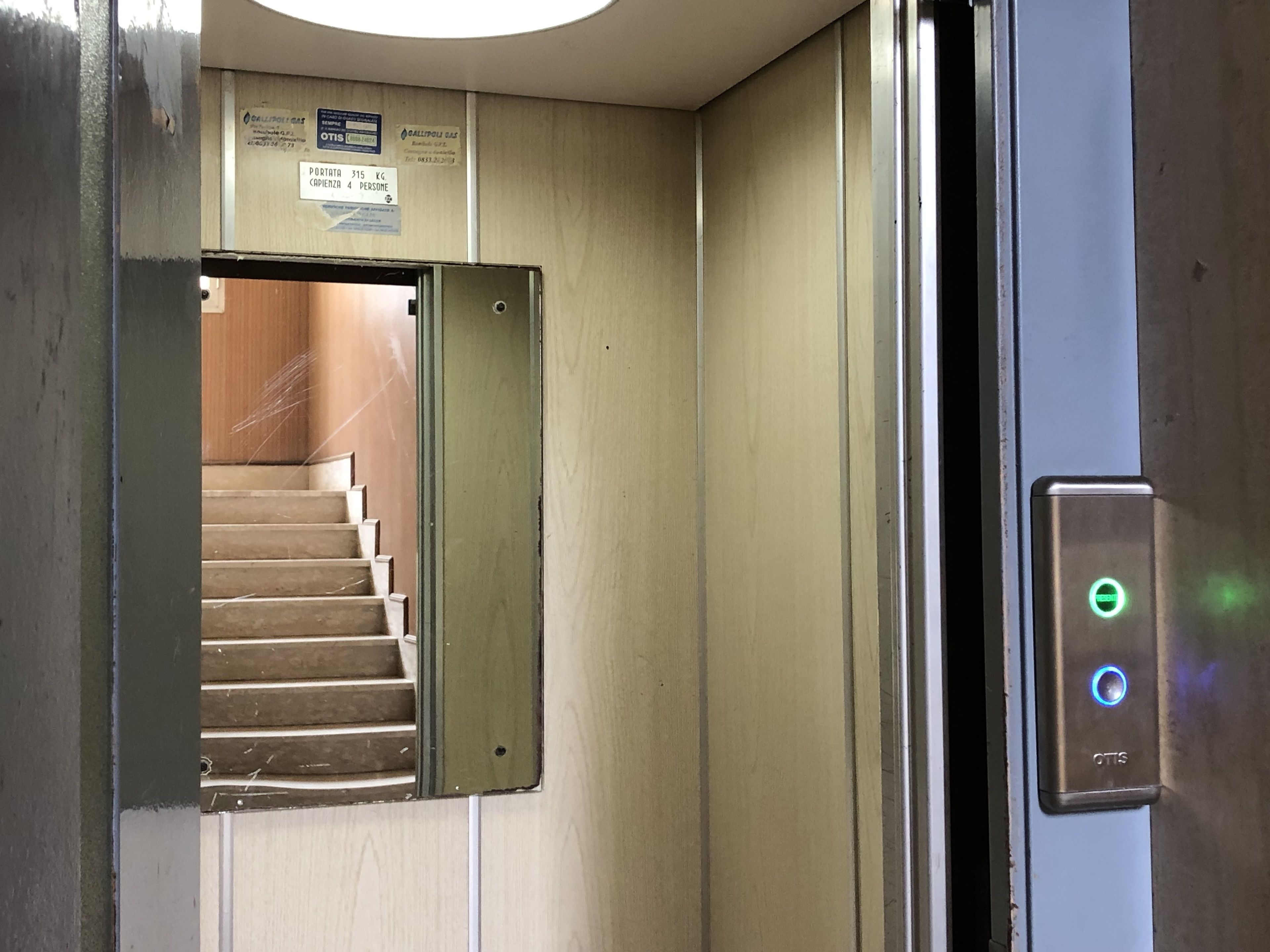An elevator with a control panel displaying a green light and a button labeled "OTTS".