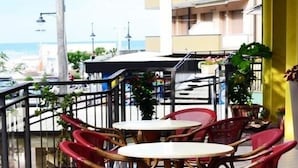A balcony with two round tables and red chairs, overlooking a street with cars and buildings. - Hotel Abel (Cesenatico)