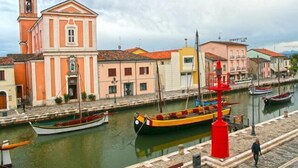 A waterfront with a church, boats, and a red lamp post. - Hotel Abel (Cesenatico)