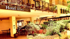 A hotel interior with a sign reading "Hotel Abel". There are outdoor seating areas with tables and chairs, and a decorative planter with plants. - Hotel Abel (Cesenatico)