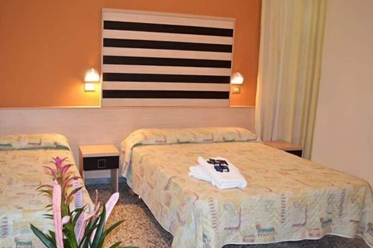 A hotel room with two single beds, a nightstand, a lamp, and a potted plant.