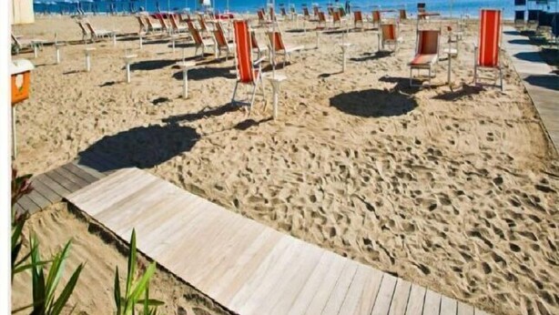 A beach with rows of sun loungers and umbrellas, a wooden boardwalk, and a clear view of the sea. - Hotel Abel (Cesenatico)