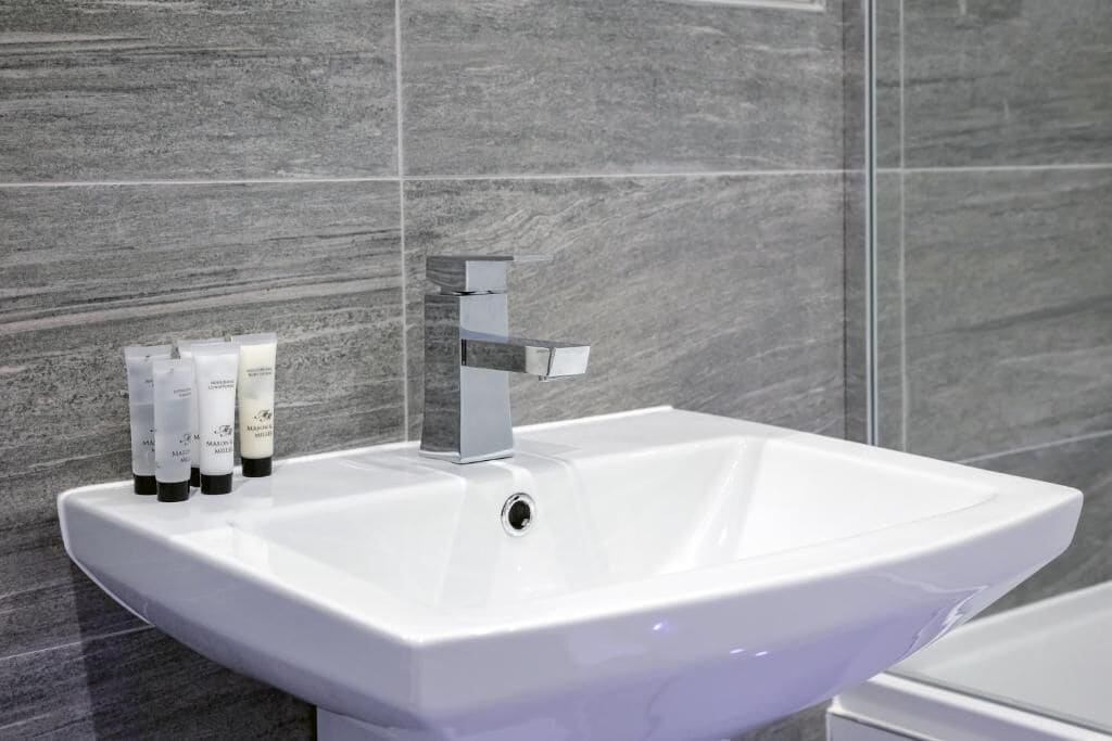 A white sink with a modern faucet and three bottles of skincare products on the countertop.