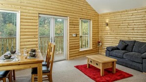 A log cabin interior with a dining table set, a sofa, and a red rug. - Canada Lodge and Lake (Cardiff)