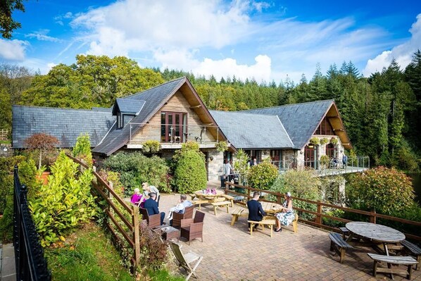 A lodge with two main buildings, outdoor seating, and a forested backdrop. - Canada Lodge and Lake (Cardiff)