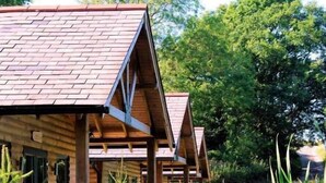 A wooden cabin with a sloped roof, a covered porch, and a pathway leading to a small dock over water. - Canada Lodge and Lake (Cardiff)