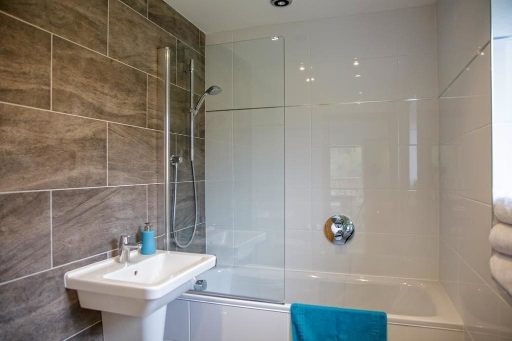 Une salle de bain moderne avec une douche à l’italienne en verre, un lavabo blanc et une baignoire.