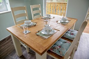 A dining table set for four with white chairs, a wooden table, and a view of a wooden deck outside. - Canada Lodge and Lake (Cardiff)