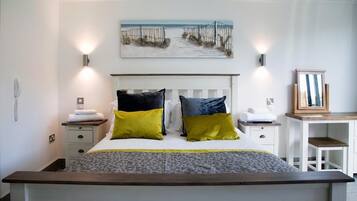 A bedroom with a white bed, two bedside tables, a headboard, a painting above the bed, and a small table with a framed picture.
