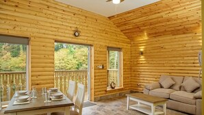 A log cabin with a dining area, a sofa, and a view of the forest. - Canada Lodge and Lake (Cardiff)