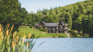 A large stone building with a balcony, surrounded by a lush green landscape and a lake. - Canada Lodge and Lake (Cardiff)