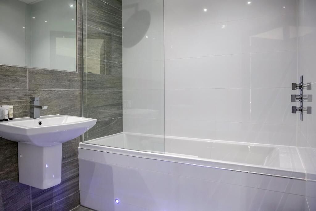 A modern bathroom with a white sink, a glass shower enclosure, and marble walls.