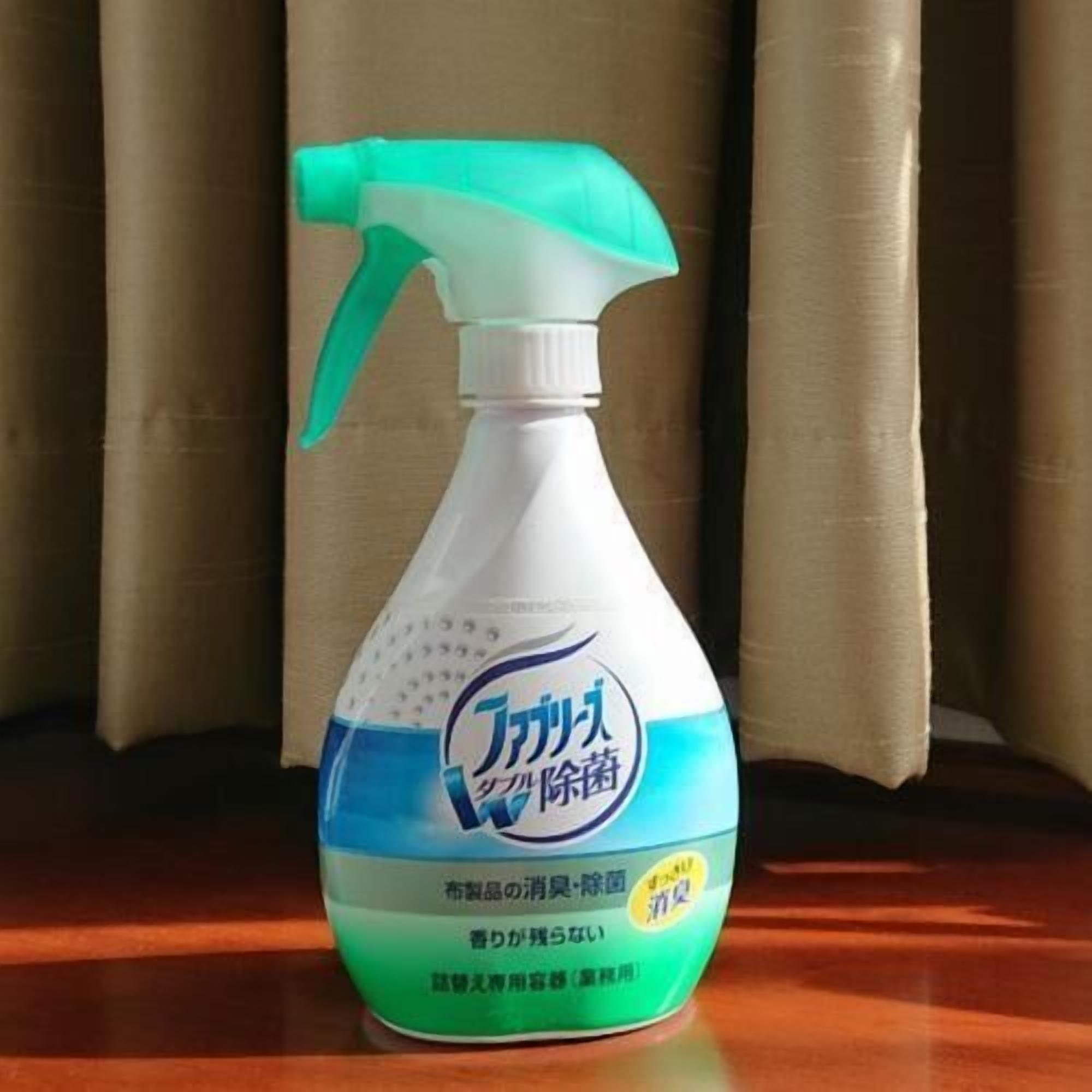 A spray bottle with a label, placed on a wooden surface with curtains in the background.