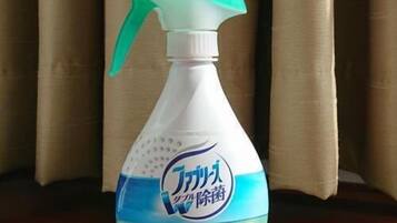 A spray bottle with a label, placed on a wooden surface with curtains in the background.