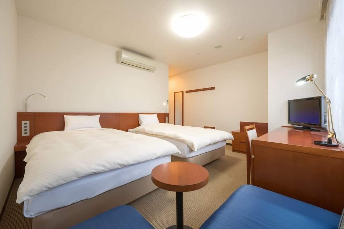 A hotel room with two beds, a desk with a computer, a TV, and a small round table.