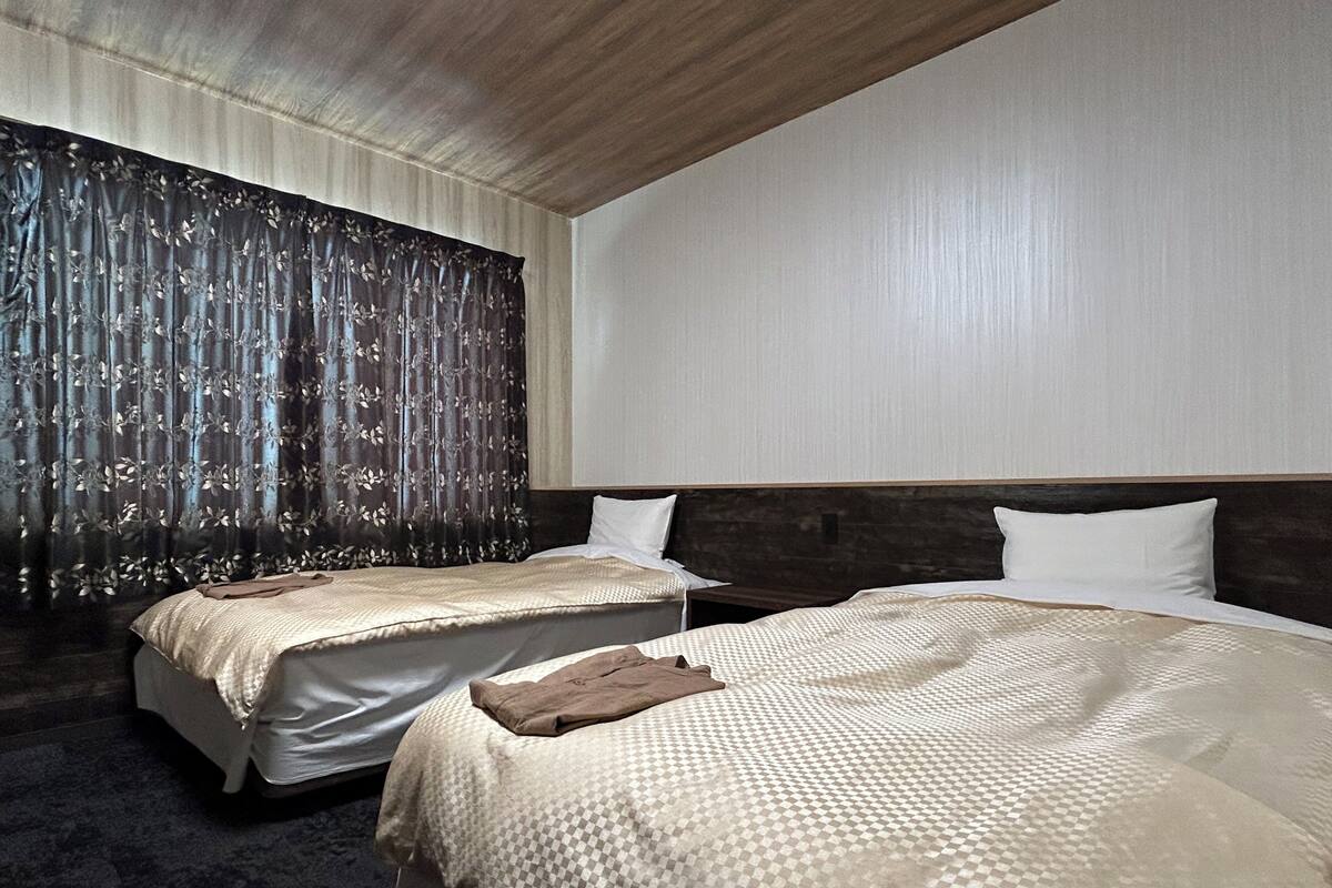 A hotel room with two beds, a large window with curtains, a wooden ceiling, and a carpeted floor.
