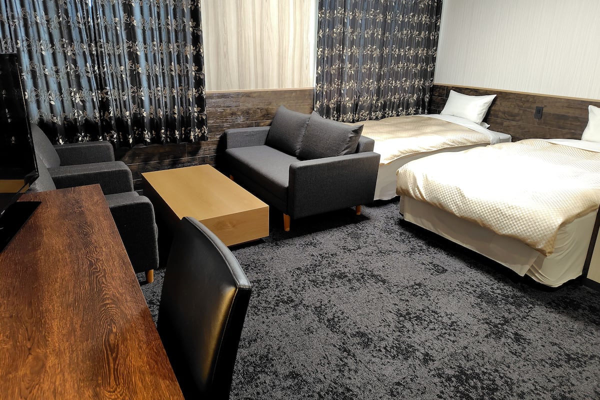A hotel room with a sofa, a bed, a wooden table, and a carpeted floor.