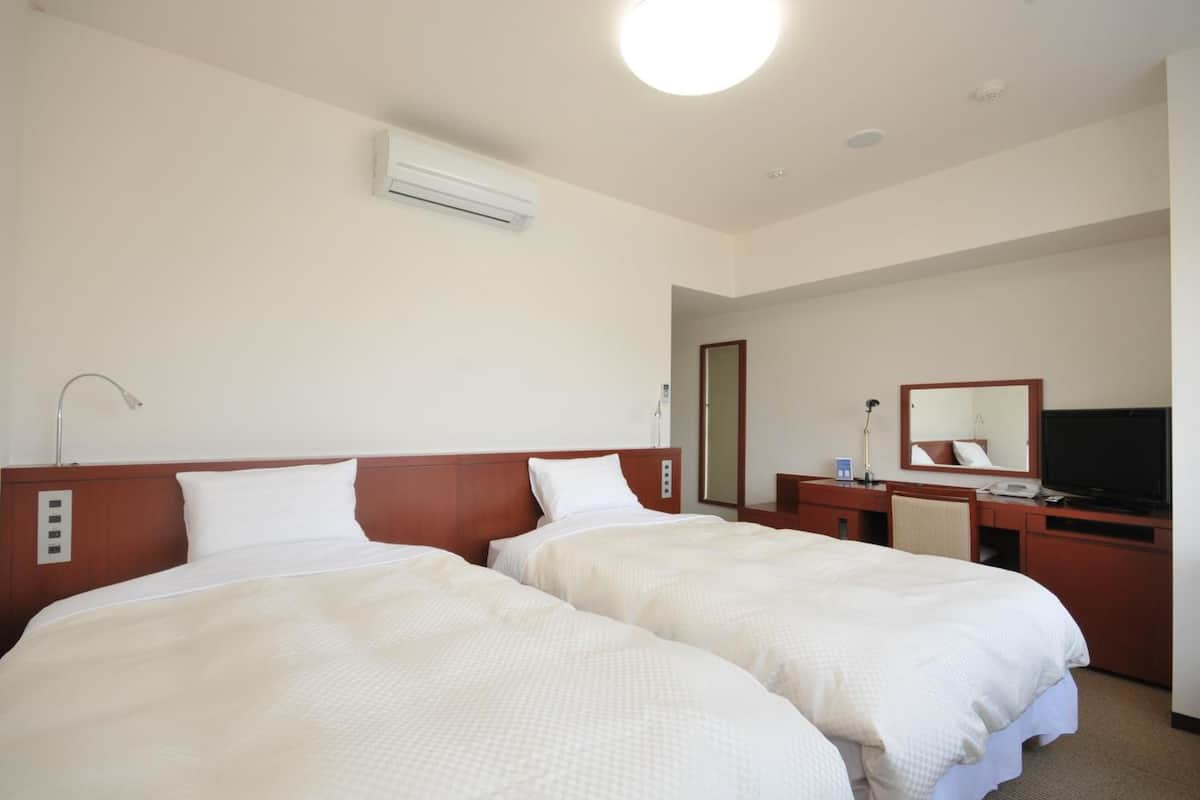 A hotel room with two beds, a desk, a television, and a mirror.