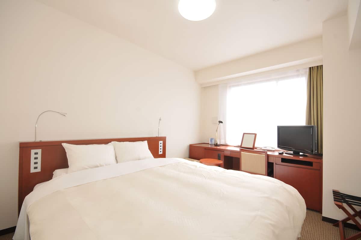 A hotel room with a large bed, a desk with a television, and a window with curtains.